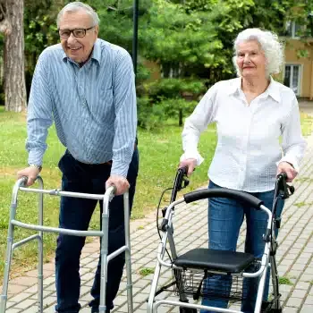 An older couple walking outdoors with a walker and rollator